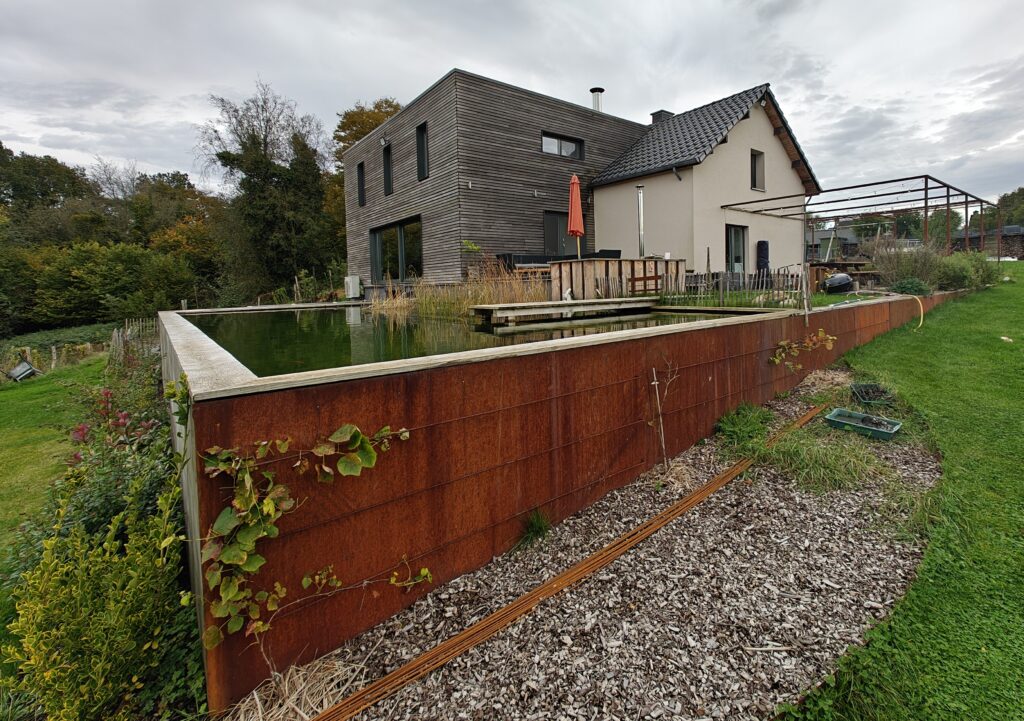 Hier is het afgewerkte bijgebouw, bekleed met houten gevelbekleding. Op de voorgrond ziet u onze natuurlijke zwemvijver met een buitenwand van cortenstaal.