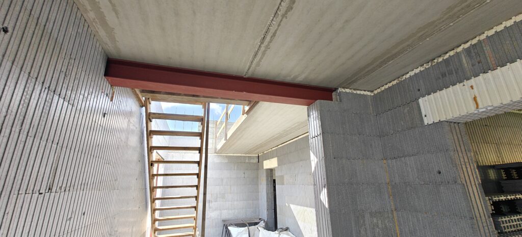 Om de werf te beveiligen, hebben we een tijdelijke houten trap geplaatst, alsook leuningen in alle zones met valgevaar. Op deze foto zie je ook een draagbalk voor de welfsels, geïntegreerd in de structuur gerealiseerd in isolerende bekistingsblokken.